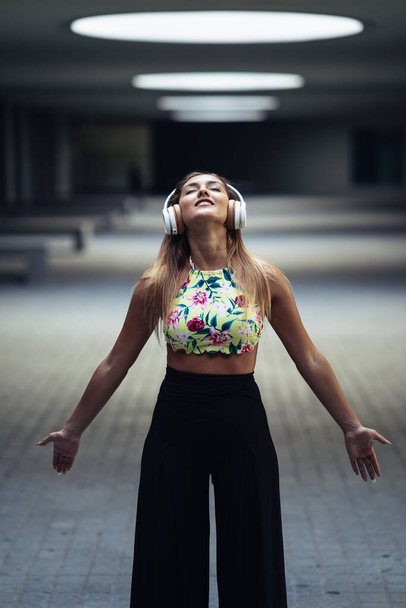 Νεαρή γυναίκα ανοίγει τα χέρια φορώντας ακουστικά σε εξωτερικούς χώρους - Φωτογραφία, εικόνα