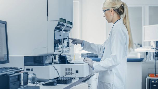 En Bio Technological Laboatory Female Research Scientist analiza el tubo de ensayo en la máquina médica, funciona con sangre, muestras de material genético. - Foto, Imagen