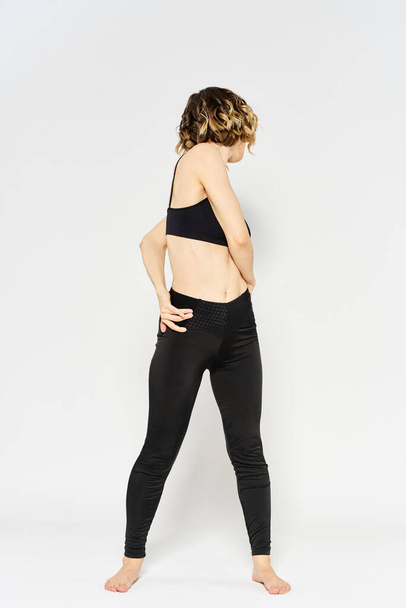 mujer deportiva en jeans negros y una camiseta haciendo ejercicios en una habitación luminosa - Foto, imagen