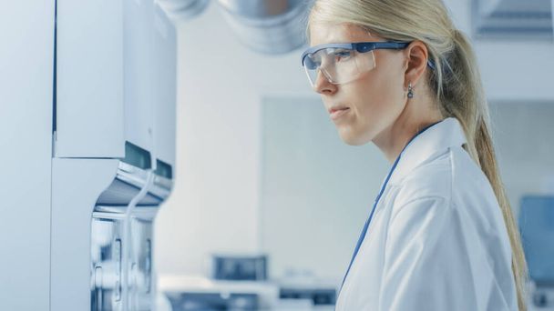 Retrato Tiro de cientista de pesquisa do sexo feminino em pé em óculos de proteção e trabalhando com equipamentos de análise médica. Trabalhos do cientista no laboratório farmacêutico moderno. - Foto, Imagem