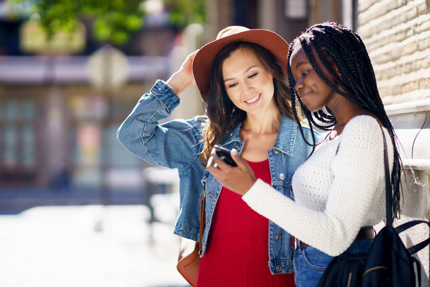 Dos amigos mirando su smartphone juntos. Mujeres multiétnicas. - Foto, Imagen