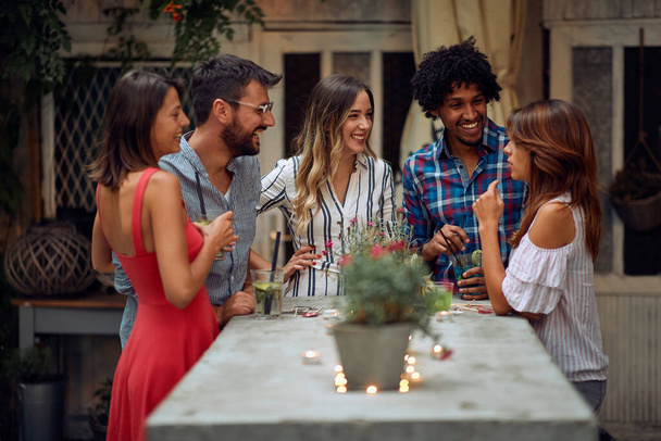 Cheerful friends enjoying a talk at the open air birthday party on a beautiful summer dusk. Quality friendship time together - 写真・画像