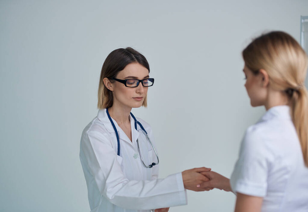 γυναίκα γιατρός σε ένα ιατρικό φόρεμα σφίγγει το χέρι με έναν ασθενή σε ένα λευκό t-shirt σε ένα ελαφρύ φόντο - Φωτογραφία, εικόνα