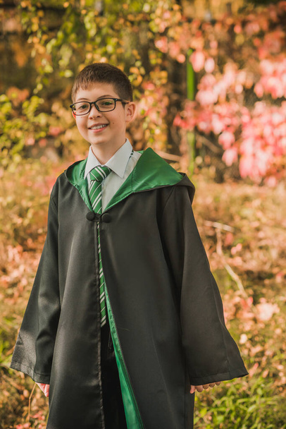 Детский волшебник. Молодой ученик волшебной школы вызывает колдовство. Мальчик в зеленом халате магия в лесу. Хэллоуин - Фото, изображение