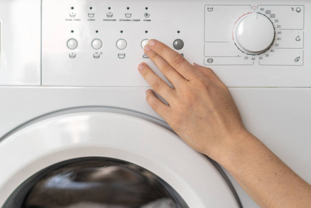 Καλλιεργημένη άποψη της γυναίκας χέρι επιλέγοντας το πρόγραμμα στον πίνακα ελέγχου στο σύγχρονο πλυντήριο ρούχων. Η νοικοκυρά πλένει τα ρούχα στο σπίτι και χρησιμοποιεί εξοπλισμό μπάνιου. - Φωτογραφία, εικόνα