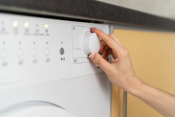 Gesneden weergave van de vrouw gereguleerde knop, het kiezen van programma op het bedieningspaneel van de moderne wasmachine. Huisvrouw doet de was thuis en het gebruik van wasmachines - Foto, afbeelding