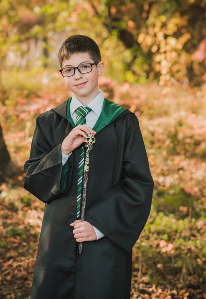 Mały czarodziej. Młody uczeń magicznej szkoły przywołuje. Chłopiec w zielonym szlafroku magia w lesie. Halloween czas - Zdjęcie, obraz