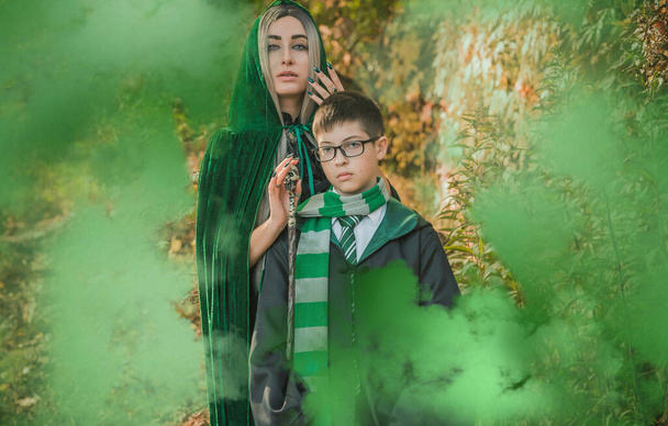 Kind und Hexe in der magischen Atmosphäre. Junge und Mutter in grünen Gewändern zaubern im Wald. Halloween-Zeit für Familien - Foto, Bild