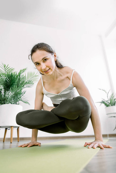 Bottom angle view of young attractive yogi woman, wearing sportswear bra and pants, practicing yoga or pilates exercise in modern studio, standing in Tolasana exercise, Scale pose - Fotografie, Obrázek