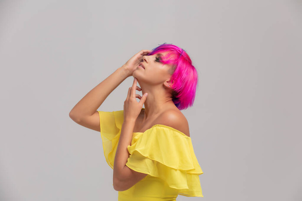 Портрет женщины с яркими цветными волосами, голубой и розовой стрижкой. девушка с короткими волосами одета в желтое платье с открытыми плечами на светлом фоне - Фото, изображение