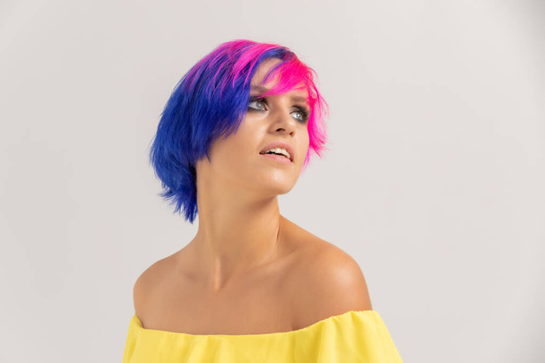 Retrato de uma mulher com cabelo colorido brilhante, corte de cabelo azul e rosa. menina com cabelo curto vestido com vestido amarelo com ombros abertos - Foto, Imagem