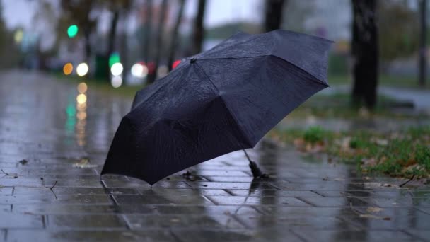 rzucony czarny parasol na drogę w deszczowy dzień - Materiał filmowy, wideo