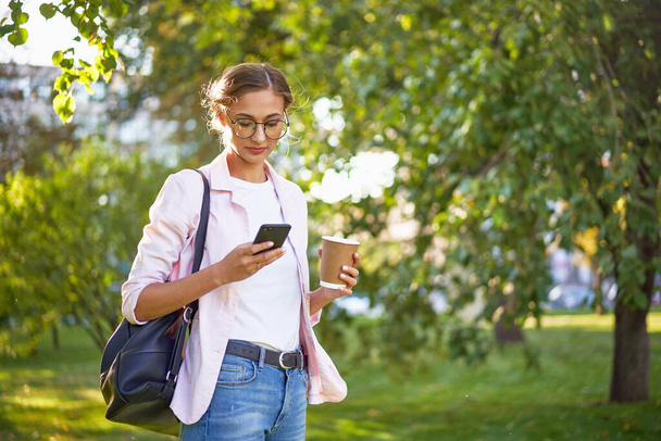 Businesswoman standing summer park Business person using smartphone Outdoors Successful european caucasian woman freelancer or teacher walking outside backpack dressed jeans white shirt pink jacket - Foto, Imagem
