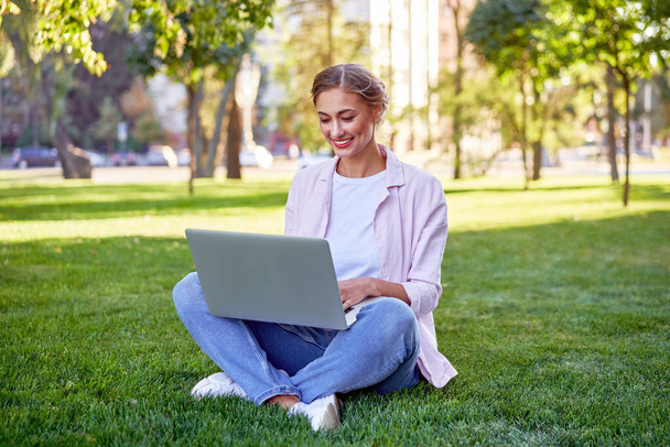 Businesswoman sitting grass summer park using laptop Business persone working remote. Outdoors Successful european caucasian woman freelancer make video call teacher study work online lessons  - Photo, image
