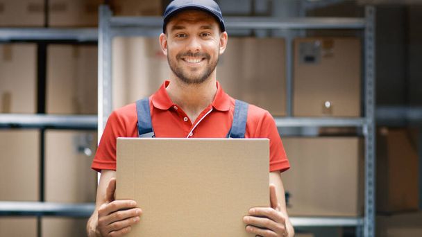 Handsome Warehouse Worker in Uniform Holds Cardboard Box Package and Smiles. - Foto, Bild