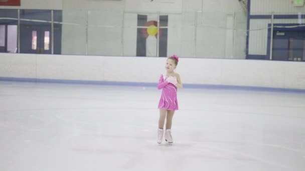Kis műkorcsolyázó rózsaszín ruhában gyakorol a fedett jégpályán.. - Felvétel, videó