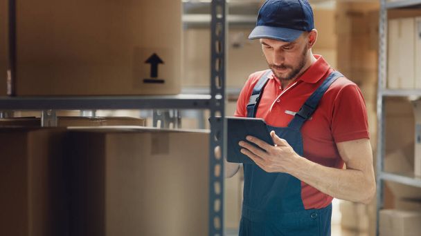 Handsome Warehouse Worker Uses Digital Tablet For Checking Stock, On the Shelves Standing Cardboard Boxes. - Φωτογραφία, εικόνα