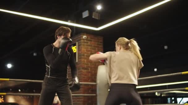 Активная спортивная пара борется в спортзале. Тренер тренирует девушку на боксерском ринге - Кадры, видео