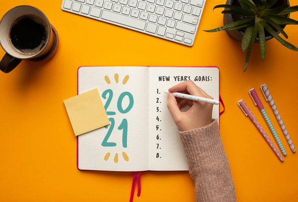 Stockfoto van vrouw schrijven doelen in een 2021 Nieuwjaar notebook op gele achtergrond - Foto, afbeelding