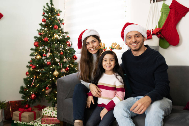 Familia hispana de tres personas que usan sombreros de Navidad y disfrutan de su tiempo juntos en casa en las fiestas - Foto, imagen