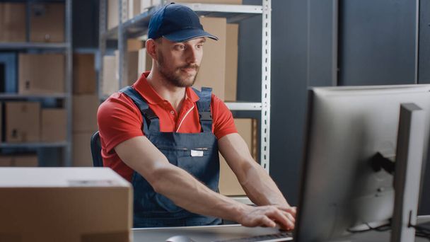 Portrait of Uniformed Worker Using Personal Computer while Sitting at His Desk in the Warehouse. - Φωτογραφία, εικόνα