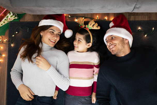 Cute happy Latin family of three laying on the floor at home and having a good time together on Christmas - Photo, Image