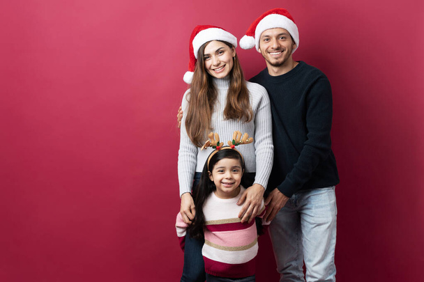 Portrait d'une belle famille latine portant des chapeaux de Père Noël et sentant l'esprit de Noël dans un studio - Photo, image