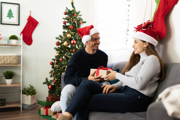Attractive Latin man handing over a Christmas gift to his partner while celebrating together at home - Fotoğraf, Görsel