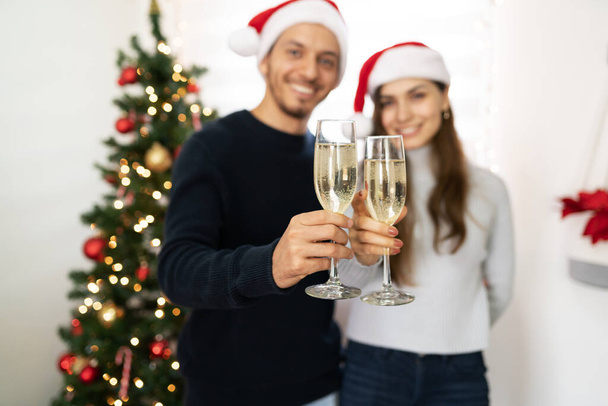 Closeup of two glasses of champagne in focus in the foreground while a couple makes a toast for Christmas - Foto, imagen