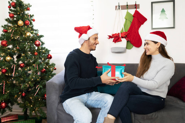 Profile view of a Latin couple exchanging and sharing Christmas gifts while celebrating at home - Fotoğraf, Görsel