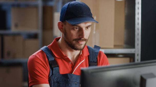 Portrait of Uniformed Worker Using Personal Computer while Sitting at His Desk in the Warehouse. - Foto, Imagen