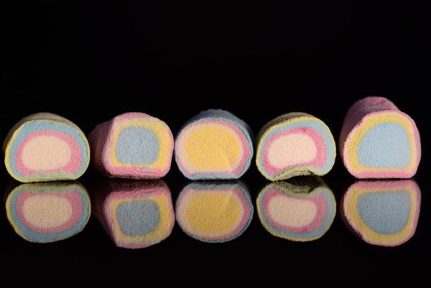 Verschillende felgekleurde marshmallows in pastelkleuren liggen naast elkaar voor een donkere achtergrond en worden gereflecteerd - Foto, afbeelding