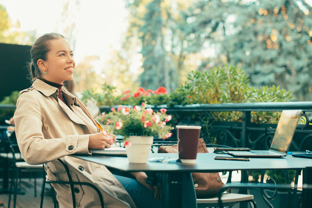 Una donna che sorride e distoglie lo sguardo è seduta a un tavolo di un caffè che lavora online - Foto, immagini