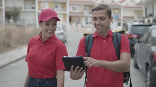 Un par de mensajeros alegres en uniformes rojos caminando afuera - Imágenes, Vídeo