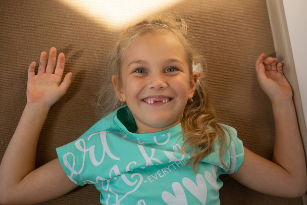 Portret zabawnej dziewczynki leży na podłodze w pokoju dziecinnym i uśmiecha się. - Zdjęcie, obraz