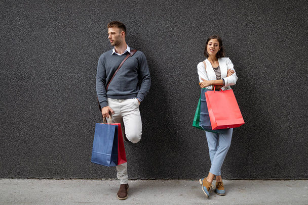 Beautiful young shopaholic woman with shopping addition. Unhappy husband man. Black friday concept. - Foto, afbeelding