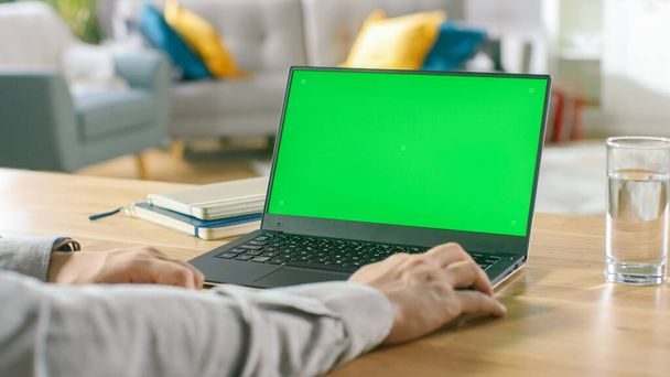 Close-up of a Man Uses Laptop with Green Mock-up Screen While Sitting at the Desk in His Cozy Living Room. - Foto, Imagem