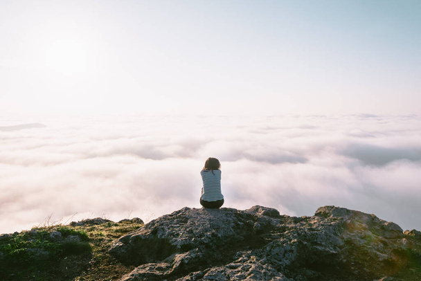 Kadın kaya yüzeyinde oturur ve bulutlarla çevrili olarak sağ tarafa bakar. Olumlu hayal ve karar verme kavramı. - Fotoğraf, Görsel