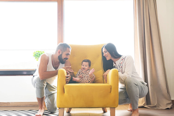 Liefdevolle ouders besteden vrije tijd met schattige kleine dochter op fauteuil thuis - Foto, afbeelding