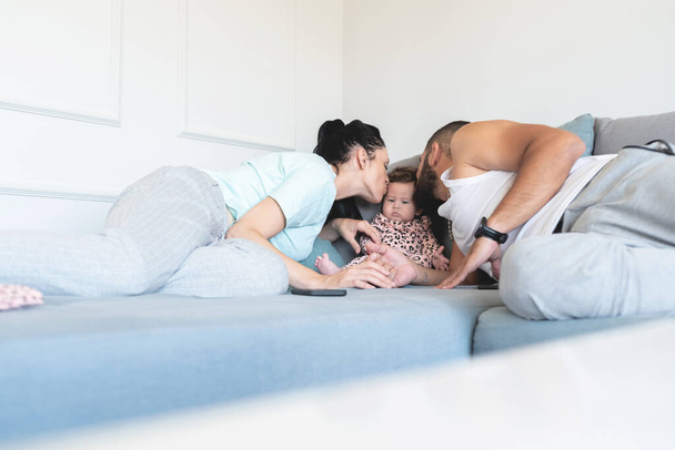 Loving parents kissing adorable baby daughter on sofa at home - Foto, afbeelding