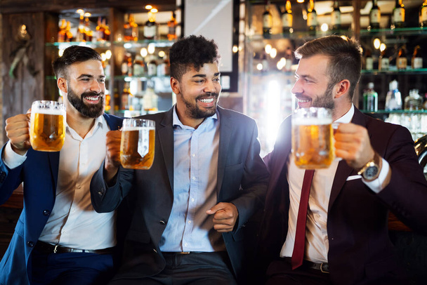 Guapos hombres de negocios bebiendo cerveza, hablando y sonriendo mientras descansan en el pub - Foto, imagen