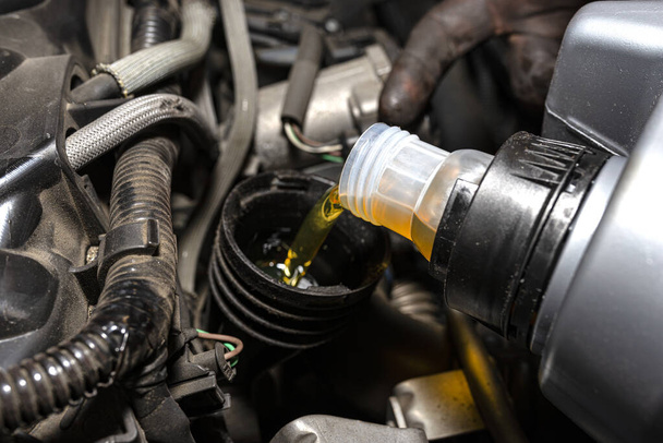 Meccanico auto versa nuovo olio per auto nel motore da un serbatoio di plastica in un'officina auto. - Foto, immagini