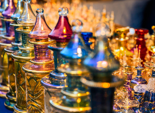 Dicht bij elkaar staan rijkelijk versierde en gekleurde parfumflacons van glas in het licht van de ondergaande zon. - Foto, afbeelding