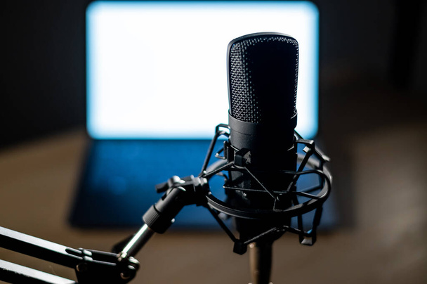 Professional microphone and laptop with white screen in the dark. Equipment in a recording and broadcasting studio - Φωτογραφία, εικόνα