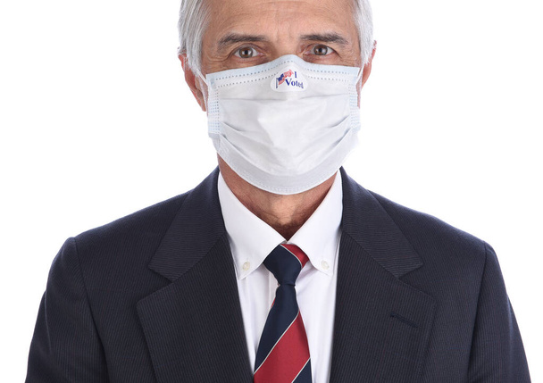 Closeup of a businessman with an I Voted sticker on the COVID-19 protective mask he wore to vote. - 写真・画像