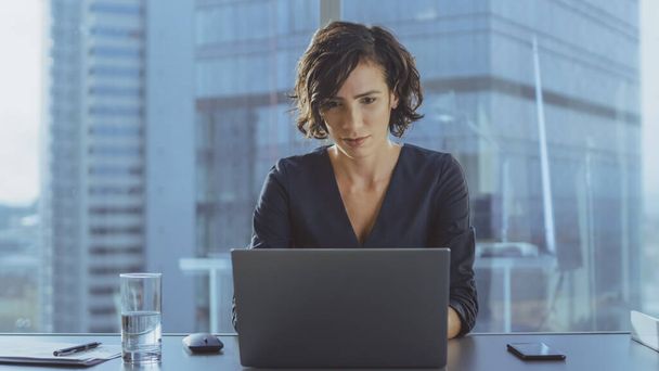 Beautiful Successful Female CEO Works on a Laptop in Her Modern Sunny Office with Cityscape Window View. Strong Female Business Leader. - 写真・画像