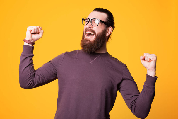 Excited young bearded man with glasses is screaming of cheerfulness and is holding his both hands up - Foto, Imagem
