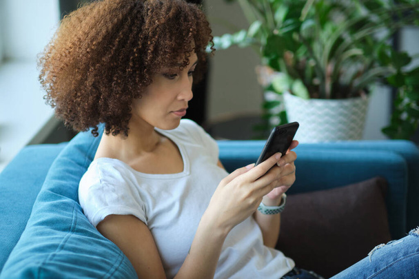 personas, la tecnología y el concepto de ocio primer plano de feliz afroamericana joven mujer mensajes de texto en el teléfono inteligente en casa - Foto, Imagen