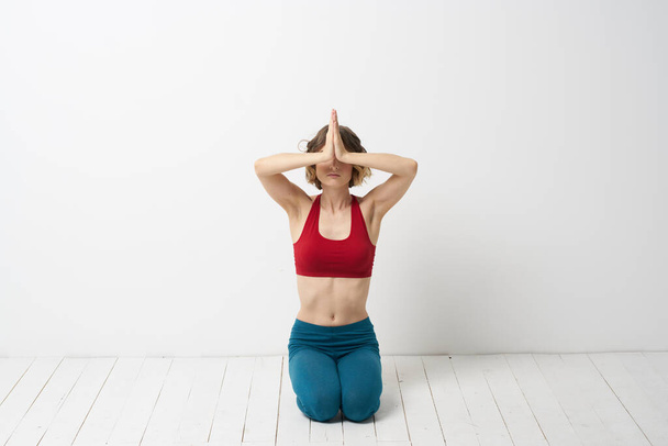 A woman in blue jeans practices yoga on a light background indoors and a slim figure in gymnastics - Foto, immagini