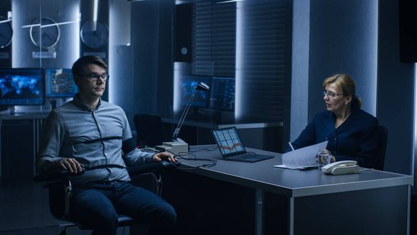 Female Special Agent Conducts Lie Detector Polygraph Test on a Young Suspect. Expert Examiner Questions Accused in Interrogation Room Writes Down Reactions. - Foto, afbeelding